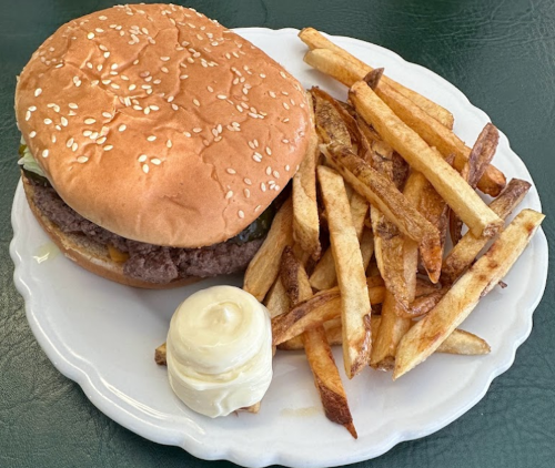 A sesame seed bun burger with a beef patty, served with a side of golden fries and a dollop of mayonnaise.